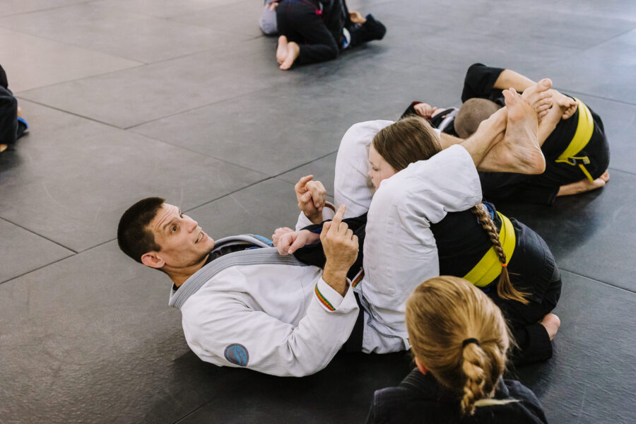 Black belt professor Matt Vernon teaches young girls in kids BJJ class at Primate Jiu Jitsu how to properly secure and finish the triangle choke strangle submission