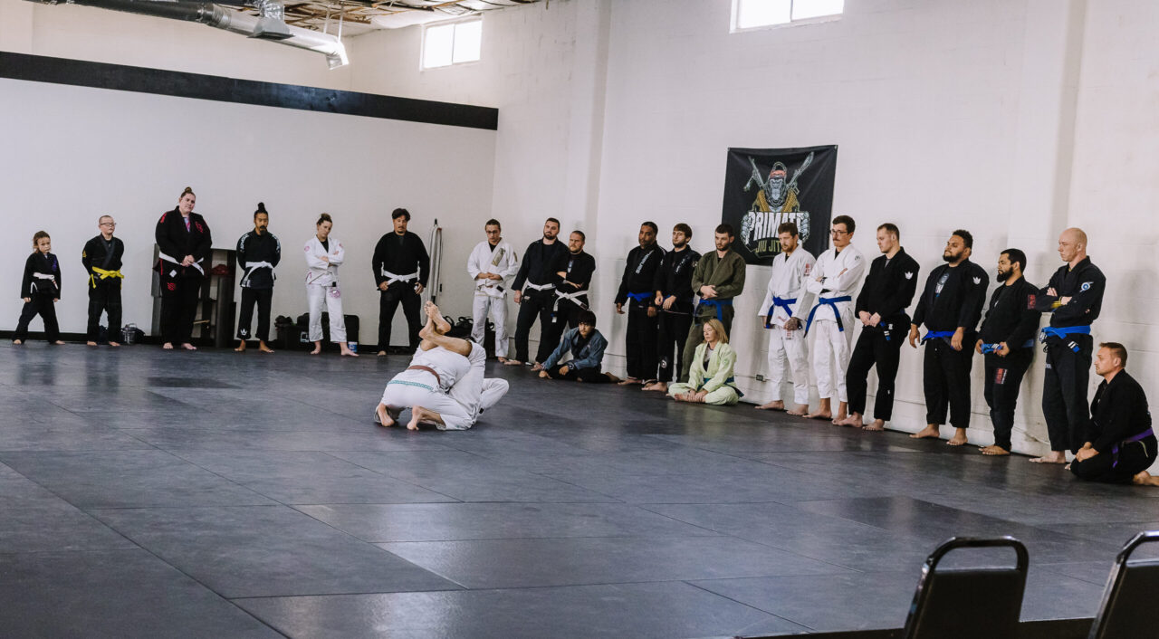 Black belt professor Matt Vernon demonstrates closed guard attacks using the gi kimono on female instructor Kendall Vernon during adult BJJ class at Primate Jiu Jitsu in Tulsa OK