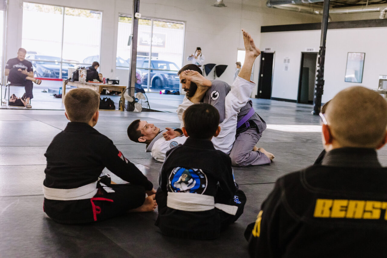 Black belt professor Matt Vernon demonstrates an arm bar submission attack from the closed guard on purple belt assistant coach Chris Stafford during a kids BJJ class at Primate Jiu Jitsu in Tulsa OK