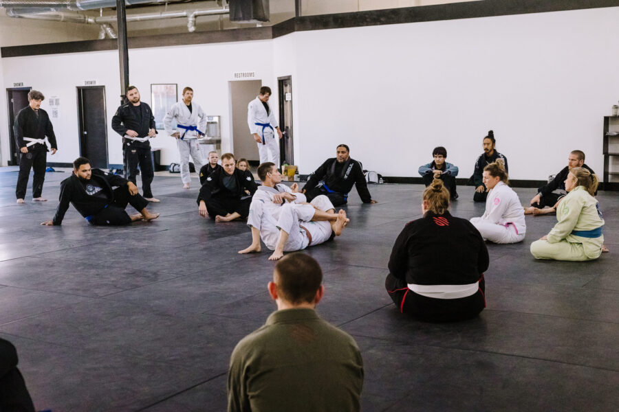 Black belt professor Matt Vernon demonstrates closed guard attacks using the gi kimono on female instructor Kendall Vernon during adult BJJ class at Primate Jiu Jitsu in Tulsa OK