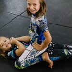 Two girls ages 7 and 8 train nogi grappling together at Primate Jiu Jitsu in Tulsa OK during kids class wearing youth Gaidama BJJ gear made for girls