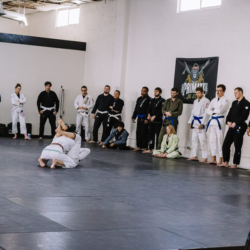 Black belt professor Matt Vernon demonstrates closed guard attacks using the gi kimono on female instructor Kendall Vernon during adult BJJ class at Primate Jiu Jitsu in Tulsa OK